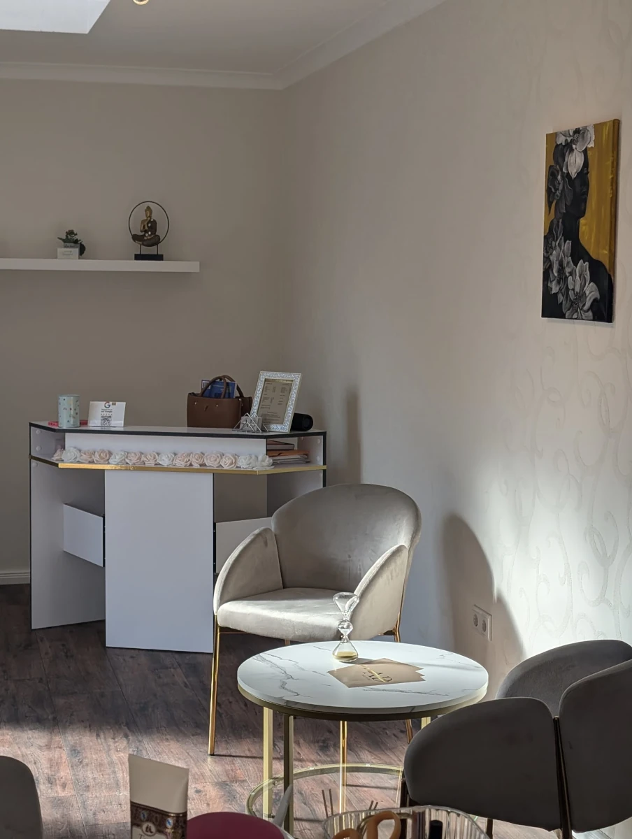 alisha-danielyan-nail-studio-wartebereich-näher-kleiner a chair and table in a room with a picture on the wall and sun rays